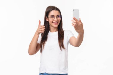 İletişim, teknoloji ve yaşam tarzı kavramı. Neşeli, mutlu, gözlüklü, gülümseyen beyaz kız portresi, selfie çeken internet blogcusu, takipçilerine video mesajı kaydeden, telefonu tutan