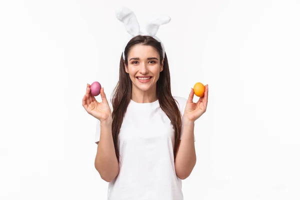 Portrait de belle femme caucasienne dans les oreilles de lapin, montrant deux œufs colorés et souriant, féliciter tout le monde avec heureux jour de Pâques, célébrer et avoir du plaisir, fond blanc — Photo