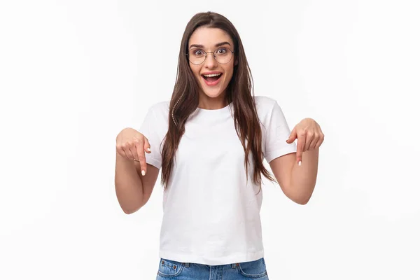 Waist-up portrait of excited young pretty woman seeing fantastic news, event promo or special spring discount, pointing fingers down and looking camera enthusiastic, stand white background — Stock Photo, Image