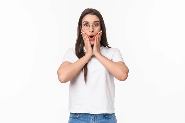 Retrato en la cintura de la excitada mujer morena caucásica curiosa en gafas, escuchar noticias increíbles, fascinado y emocionado mirando cámara, decir wow touch mejillas impresionado, fondo blanco —  Fotos de Stock