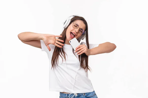 Technology, lifestyle and music concept. Carefree, enthusiastic young chilling woman having fun, girl dancing to favorite song, sing along in mobile phone like mic, listening in headphones — Stock Photo, Image