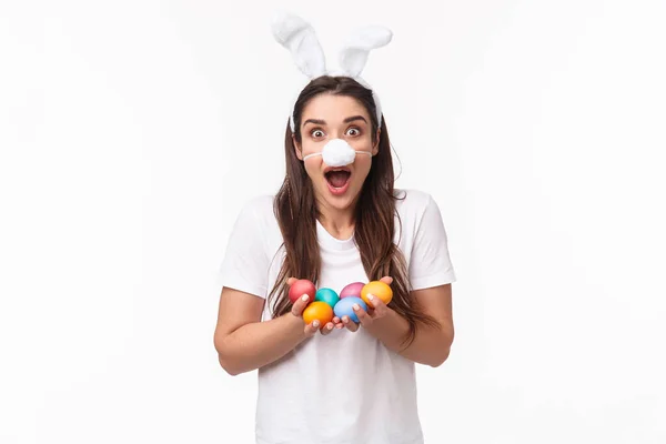 Portrait de jeune femme heureuse et excitée portant costume de lapin, oreilles et masque de nez moelleux, tenant des œufs colorés, célébrant fête de Pâques de vacances, stand fond blanc étonné — Photo