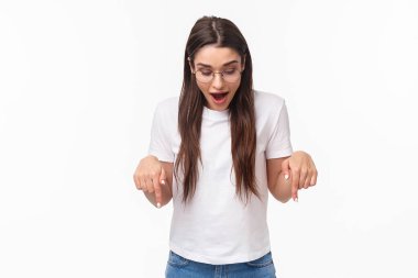 Şaşkın, meraklı, tişörtlü, gözlüklü, neşeli esmer kadının portresi. Eğlenceye bakıyor ve işaret ediyor. Alttaki tanıtımda muhteşem bir şey görüyor.