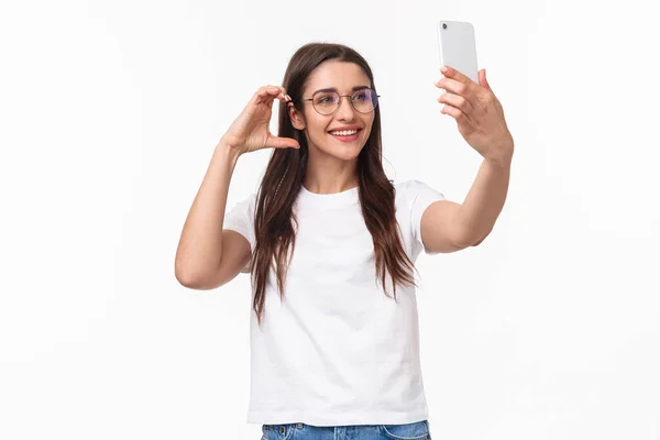 Kommunikation, Technologie und Lifestylekonzept. Porträt einer charmant lächelnden jungen Frau mit Brille, die ein Selfie mit dem Handy macht und versucht, ein hübsches Foto für die sozialen Medien zu machen — Stockfoto