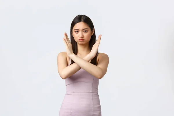 Mujeres de lujo, fiesta y concepto de vacaciones. Mujer asiática seria en vestido de noche haciendo gesto cruz, decir que parar, prohibir o restringir, de pie fondo blanco renuente —  Fotos de Stock