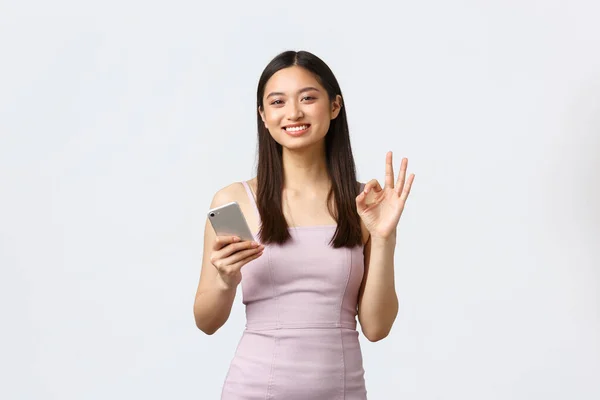 Menina asiática jogando emocionalmente no smartphone em jogo online isolado  em fundo colorido expressão de rosto alegre