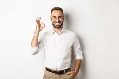 Tatmin olmuş iş adamı gülümsüyor ve işaret veriyor, onaylıyor ve beyaz arka planda duran iyi bir şey gibi.