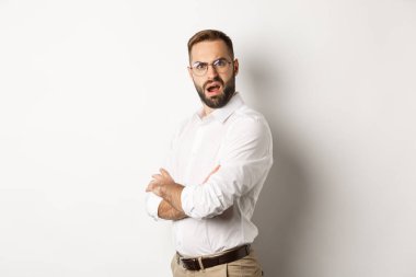 Kafası karışmış yönetici kameraya bakıyor, beyaz arkaplana karşı şokta.