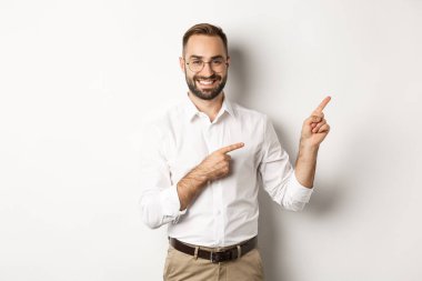 Yakışıklı ve başarılı bir iş adamı, sağı işaret ediyor, memnun yüzlü, beyaz arkaplan reklamını yapıyor.