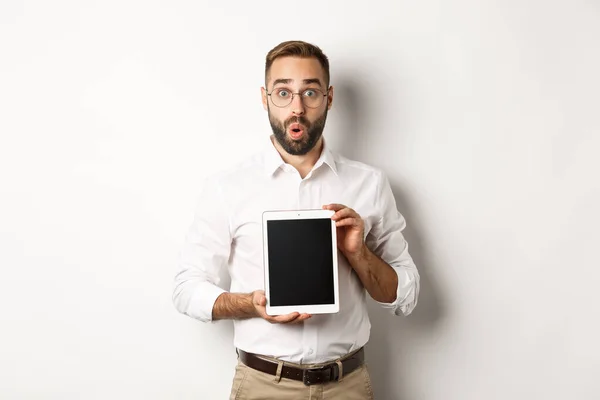 Homme surpris dans des lunettes, montrant l'écran de la tablette numérique, regardant étonné, debout sur fond blanc — Photo