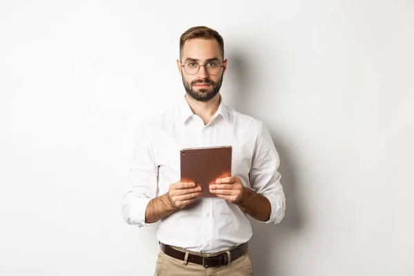 Seriös arbetsgivare som arbetar med digital surfplatta, läsning i glasögon, stående över vit bakgrund — Stockfoto