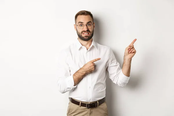 Tvivelaktig och orolig man ser obeslutsam, pekar på övre högra hörnet tveksam, står över vit bakgrund — Stockfoto