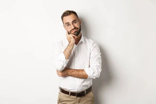 Unamused bärtiger Mann mit Brille blickt missmutig in die Kamera, steht launisch über weißem Hintergrund — Stockfoto