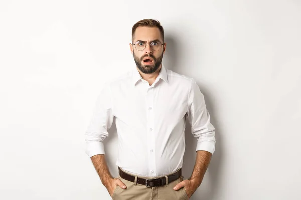 Chocado e descontente empresário em óculos, ofegante e olhando chateado para a câmera, em pé sobre fundo branco — Fotografia de Stock