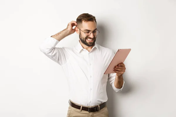 Verward mannelijk manager kijken verbaasd op digitale tablet, krabben hoofd twijfelachtig, staande over witte achtergrond — Stockfoto