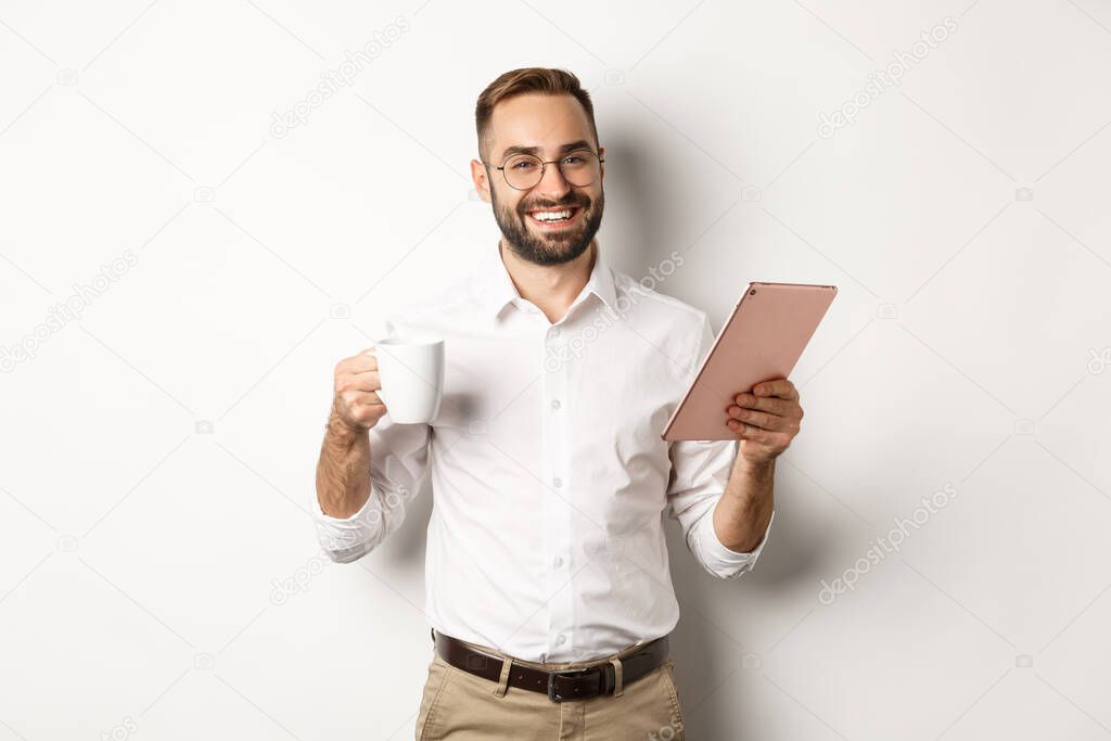 Satisfied boss drinking tea and using digital tablet, reading or working, standing over white background