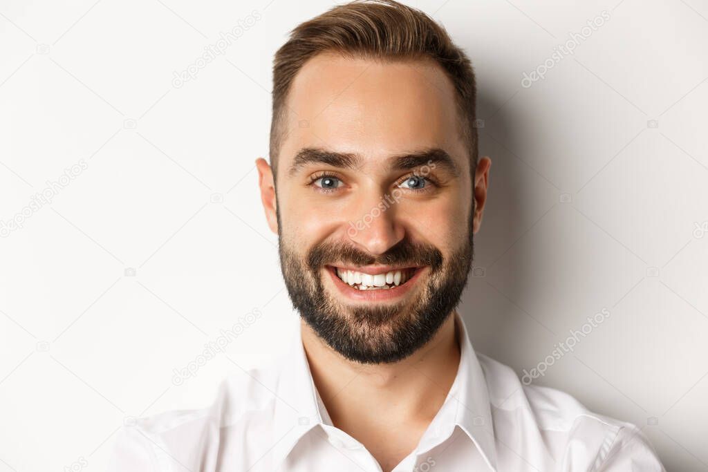 Headshot of handsome bearded man smiling, standing against white background