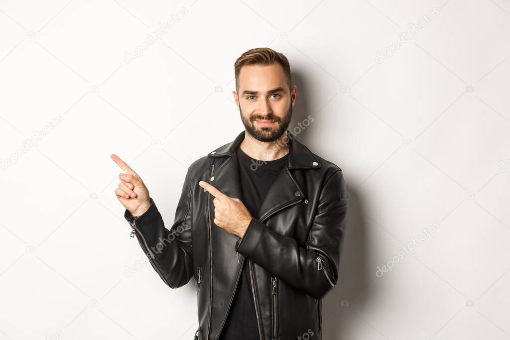 Confident macho man in black leather jacket, pointing fingers left at promo offer, showing logo, white background.