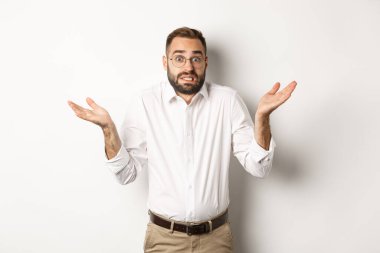 Kafası karışık görünen, beyaz arka planda duran bilgisiz, endişeli yönetici omuz silkiyor.