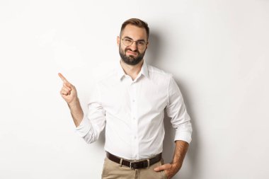 Şüpheci erkek girişimci somurtuyor, hoşnutsuz bir yüzle sol parmakla işaret ediyor, üründen şikayet ediyor, beyaz arka plan