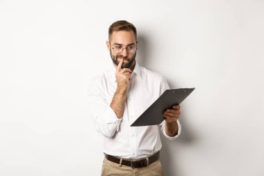 Düşünceli bir çalışan panoya bakıyor, şüpheleri var, beyaz arka planda duruyor.