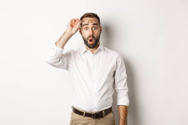 Şaşırmış iş adamı kameraya hayranlıkla bakıyor, beyaz arka planda dikiliyor.