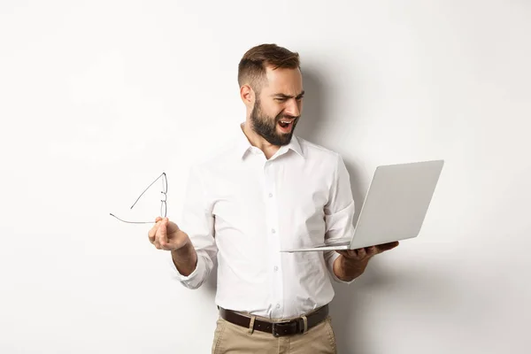 Verwirrter Manager blickt auf Laptop, steht enttäuscht vor weißem Hintergrund — Stockfoto