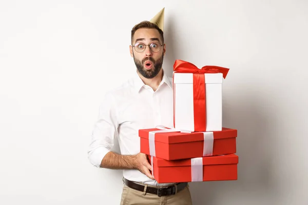 Праздники и праздники. Счастливый человек получает подарки на день рождения, держит подарки и выглядит взволнованным, стоя на белом фоне — стоковое фото