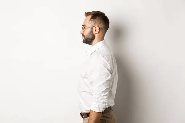 Profiili nuori liikemies valkokauluspaita ja beige housut, katsot vasemmalle, seisoo vasten studio tausta — kuvapankkivalokuva