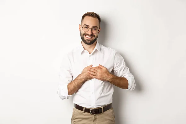 Tocado e agradecido homem de negócios de mãos dadas no coração, sorrindo grato, de pé contra fundo branco — Fotografia de Stock