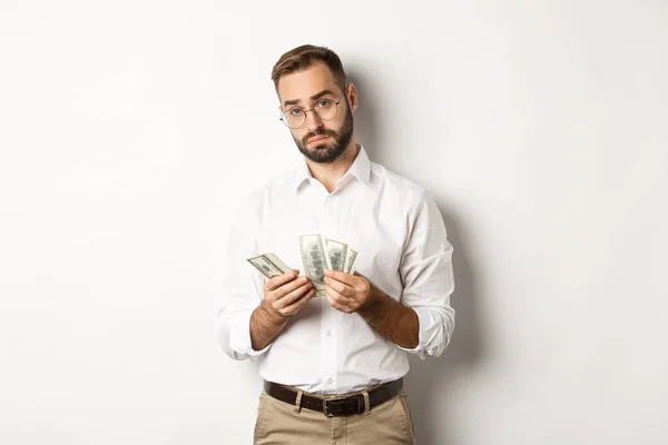 Snygg affärsman räkna pengar och titta på kameran, står allvarliga mot vit bakgrund — Stockfoto