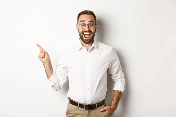 Homem surpreso e animado fazendo anúncio. Empresário apontando o dedo esquerdo no espaço de cópia, fundo branco — Fotografia de Stock