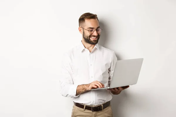 Zaken. Knappe zakenman die aan laptop werkt, berichten beantwoordt en lacht, over een witte achtergrond staat — Stockfoto