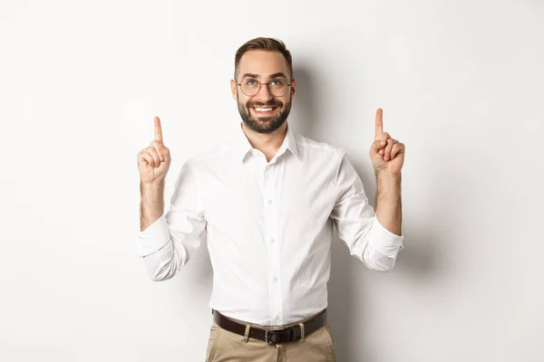 Empresário bonito confiante mostrando logotipo, apontando e olhando para cima no anúncio, de pé sobre fundo branco — Fotografia de Stock