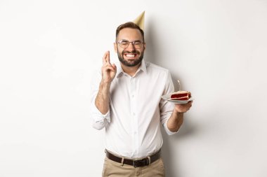 Tatiller ve kutlamalar. Doğum günü pastasında dilek tutan mutlu bir adam, çapraz parmaklar ve gülümseyen heyecanlı, doğum günü partisi veren, beyaz arka plan