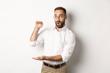 Büyük nesneler gösteren hayret verici iş adamı, beyaz arka planda duran, büyük ve heyecanlı görünen bir şey tarif et.