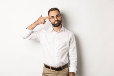 Kafasına ateş eden yorgun bir adam, sıkılmış görünüyor, beyaz arka planda sıkıntılı duruyor.