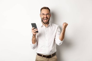 Başarılı iş adamı mutlu görünüyor, yumruk tokuşturuyor ve online piyangoyu kazanmaktan zevk alıyor, beyaz arka planda duruyor.
