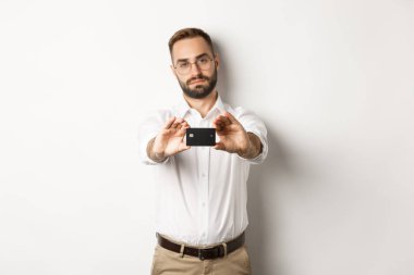 Kredi kartı gösteren ciddi bir işadamı, beyaz arka planda duruyor.