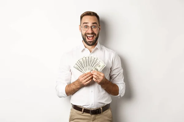 Emocionado hombre guapo sosteniendo el dinero, regocijo de ganar el premio en efectivo, de pie sobre fondo blanco — Foto de Stock