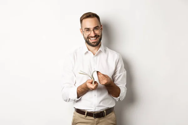 Empresário bem sucedido em camisa branca, contando dinheiro e sorrindo satisfeito, de pé sobre fundo branco — Fotografia de Stock