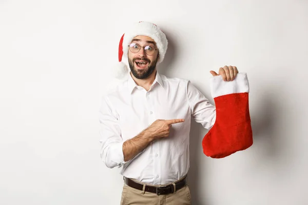 Frohe Weihnachten, Feiertage Konzept. Glücklicher erwachsener Mann erhält Geschenke in Weihnachtssocke, sieht aufgeregt aus, trägt Weihnachtsmütze, weißer Hintergrund — Stockfoto