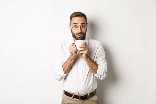 Glad kontorsarbetare dricker varmt kaffe och ser upphetsad, skvallrar, står över vit bakgrund — Stockfoto