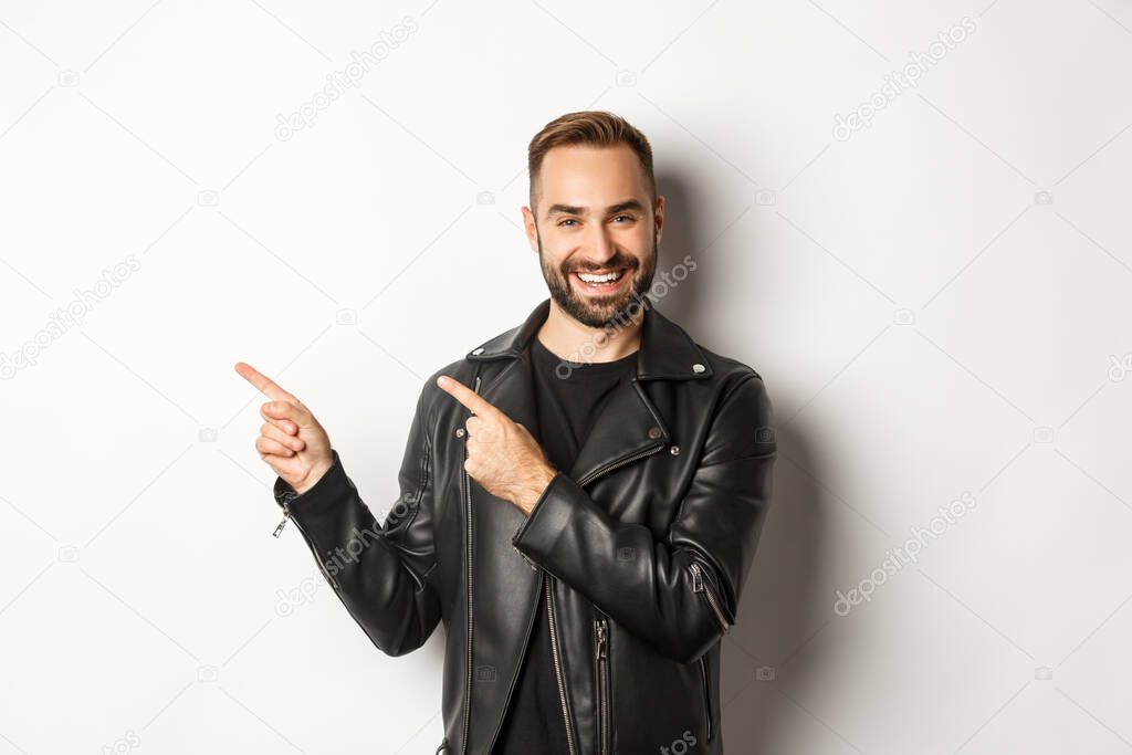 Confident macho man in black leather jacket, pointing fingers left at promo offer, showing logo, white background.