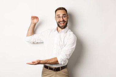 Büyük nesneler gösteren hayret verici iş adamı, beyaz arka planda duran, büyük ve heyecanlı görünen bir şey tarif et.
