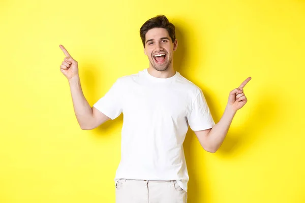 Cara elegante feliz mostrando duas variantes, apontando os dedos para os lados na promo esquerda e direita, de pé sobre fundo amarelo — Fotografia de Stock