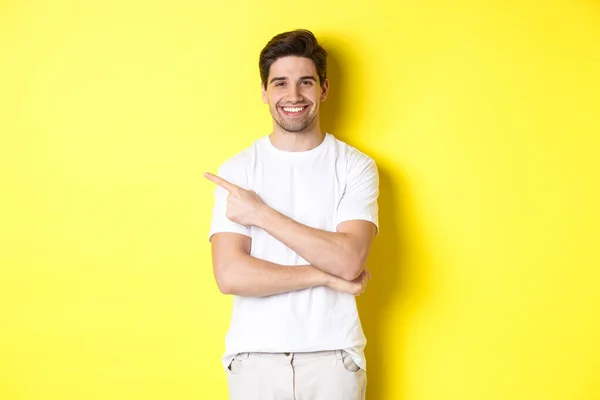 Kjekken som peker til venstre og smiler og viser reklamen på gult kopirom – stockfoto