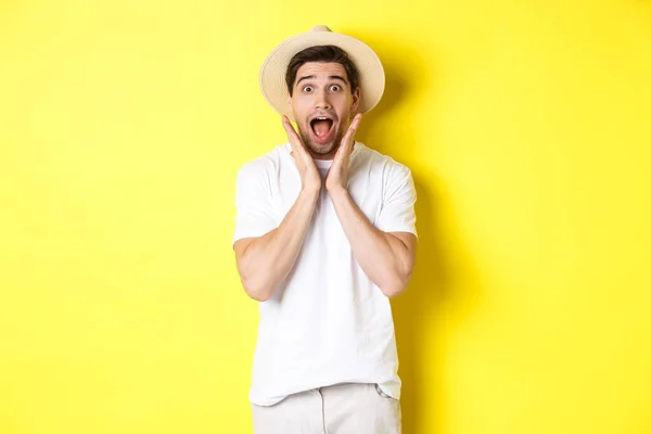 Conceito de turismo e verão. Surpreendido modelo masculino em chapéu de palha, olhando espantado com oferta especial, de pé contra fundo amarelo — Fotografia de Stock
