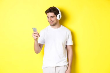 Akıllı telefondan çalma listesini seçen yakışıklı, kulaklık takan, sarı arka planda duran...