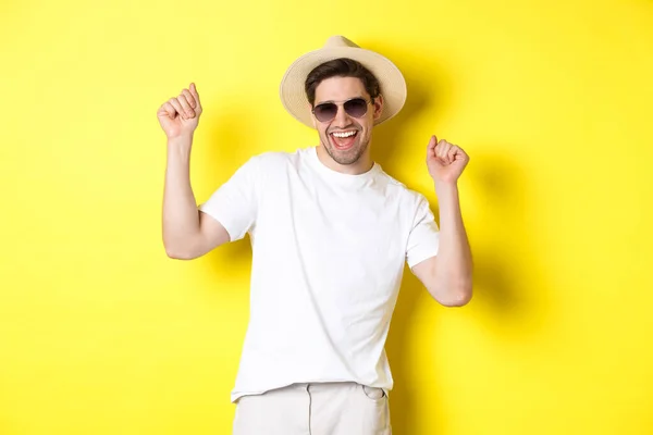 旅游、旅行和度假概念。快乐的高加索人跳舞，度假愉快，戴着墨镜，戴着草帽，站在黄色的背景下 — 图库照片